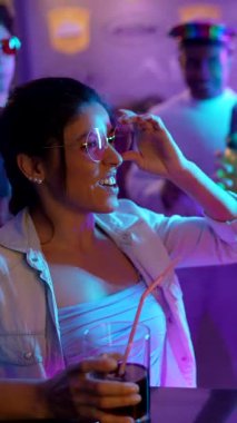 Çeşitli gülümseyen arkadaşlar dans ediyor, kokteyl içiyor ve renkli neon ışıklarla dolu canlı bir gece kulübünde birlikte kadeh kaldırıyorlar. Eğlenceli ve enerjik bir gecenin tadını çıkarıyorlar.