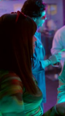 Dans eden, sosyalleşen ve dans eden renkli neon ışıklarıyla aydınlatılmış dans pistinde kokteyller içen çok kültürlü arkadaşlardan oluşan canlı bir kalabalık.