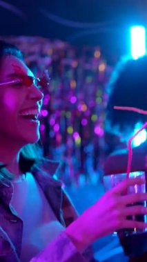 Kokteylleri olan mutlu çok ırklı kadınlar bir gece kulübünde birlikte gülüp dans ediyorlar. Eğlenceli bir hafta sonu için arkadaşlarıyla canlı mor ve mavi neon ışıklar altında kutlama yapıyorlar.