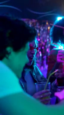 Kalabalık bir gece kulübünün neon ışıkları altında dans ederek, gülerek ve kokteyl içerek eğlenen etnik çeşitliliğe sahip mutlu bir bayan arkadaş grubu.