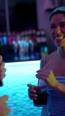 Neşeli genç bir kadın elinde bir kokteyl tutarken ve parlak bir saç bandı takarken renkli neon ışıkları olan canlı bir gece kulübü partisinde bir muhabir tarafından bir mikrofonla röportaj yapılıyor.