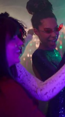 Neşeli, çok kültürlü genç kadınlar bir gece kulübü partisinde şampanya bardaklarıyla dans ediyorlar. Neşeli bir atmosferde neon ışıkları ve neşeli bir enerjiyle gülümsüyorlar.