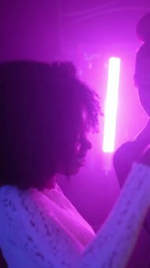 Genç çok ırklı insanlar eğleniyor, dans ediyor ve şampanya kadehleriyle kadeh kaldırıyor. Mor neon ışıklı bir gece kulübünde, göz alıcı bir atmosferde birlikte kutlama yapıyorlar.