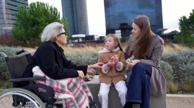 Üç kuşak ailenin birlikte dışarıda vakit geçirmesini seviyorum. Kızları ve torunları tekerlekli sandalyedeki yaşlı bir kadını ziyaret ediyor ve modern bir şehir parkında atıştırmalık bir şeyler yiyorlar.