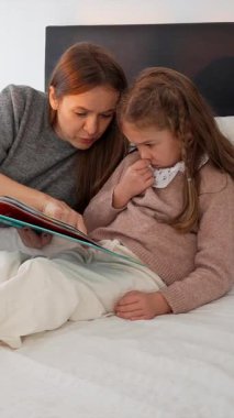 Sevgi dolu bir anne, küçük kızına masal okurken bir kitabı işaret eder. Uyumadan önce sıcak bir yatak odasında öğrenme ve kaynaşma anını paylaşır.
