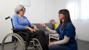 Genç bakıcı, huzurevine ya da kliniğe ev ziyareti sırasında stres topu kullanarak el rehabilitasyonu egzersizleri yapan yaşlı bir kadına yardım ediyor.