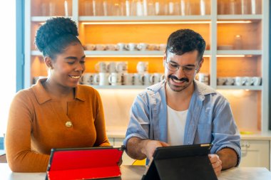 Modern bir ofis kilerinde çeşitli meslektaşlar gülümsüyor ve tabletler üzerinde işbirliği yapıyorlar, arkadaşça bir çalışma alanında gelişigüzel, verimli bir mola sırasında fikir ve planlama paylaşıyorlar.
