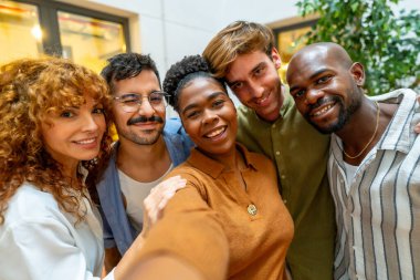 Çeşitli iş arkadaşları birlikte neşeli bir selfie çekiyorlar, takım çalışması, arkadaşlık ve modern bir çalışma alanında pozitif ofis kültürü gösteriyorlar.