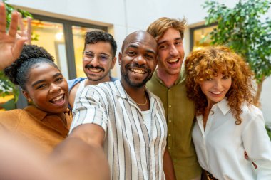 Rahatlamış bir ofis molası sırasında gülümseyen ve kameraya bakan bir grup mutlu iş arkadaşı takım çalışmasını ve bağlantıyı teşvik ediyor.