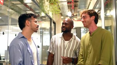 Modern bir ofis koridorunda arkadaşça sohbetin keyfini çıkaran üç farklı erkek meslektaşı hak ettikleri çalışma saatlerine ara verirken dostluk ve takım çalışmasını teşvik ediyorlar.
