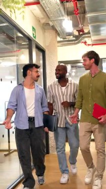 Modern bir ofis koridorunda yürüyen üç farklı ırktan erkek meslektaştan oluşan bir grup, çalışma arası sırasında arkadaşça bir sohbete giriştiler, yoldaşlığı teşvik ettiler ve olumlu bir çalışma ortamı oluşturdular.