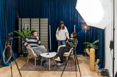 İçerik üreticileri yeni sosyal medya videoları üretiyor, genç bir kadın arkalarında profesyonel kayıt cihazları kullanarak oturup tartışırken,