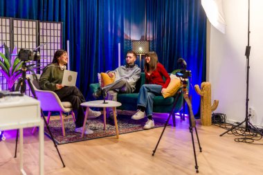 Modern bir stüdyo ortamında profesyonel ekipmanlarla bir podcast veya video röportajı kaydederken gülümseyen ve etkileşen bir grup genç içerik yaratıcısı