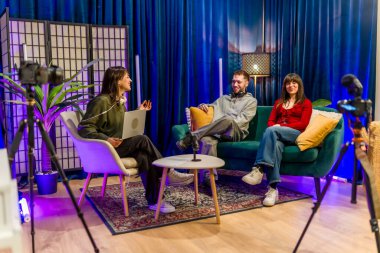 Üç genç içerik yaratıcısı, yayın için kameralar ve mikrofonlarla donatılmış modern bir stüdyoda bir podcast veya sosyal medya video röportajı kaydederek bir sohbete girişiyor.