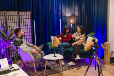 Modern bir stüdyoda kameraların, mikrofonların, aydınlatmaların ve gelişigüzel, profesyonel prodüksiyonların olduğu bir podcast ve sosyal medya videosu üzerinde çalışan çok ırklı genç yaratıcılar.