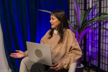 Modern bir içerik oluşturma stüdyosundan fikirleri sunan kadın, bir podcast veya canlı yayın yaparken gülümseyen ve işaret eden dizüstü bilgisayar ve profesyonel ışıklandırma ayarlarıyla