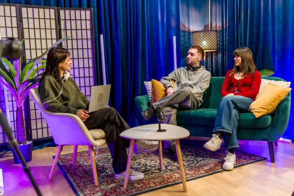 Genç erkekler ve kadınlar renkli bir stüdyo ortamında iş birliği yapıyor ve konuşuyorlar, profesyonel ekipman kullanarak bir podcast veya sosyal medya içeriği kaydediyorlar