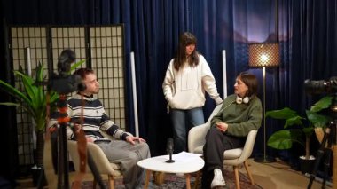 İçerik üreticileri, mikrofonlar ve kameralar da dahil olmak üzere profesyonel ekipmanlarla canlı bir podcast şovu kaydederken, bir yapımcı onlara modern yaratıcı bir stüdyo ortamında yol tarifi veriyor.