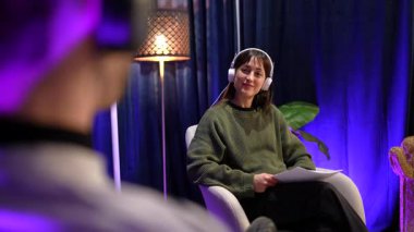 İçerik yaratan kadın bir podcast sunuyor ve sosyal medya içeriği yaratmak için profesyonel ekipmanlarla modern bir kayıt stüdyosunda canlı yayın sırasında bir konukla konuşuyor.