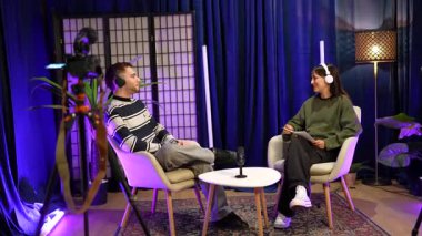 İki genç içerik yaratıcısı, bir erkek ve bir kadın, kulaklık takıyor ve profesyonel bir stüdyoda sosyal medya kanalları veya online talk show 'ları için canlı yayın sırasında oturuyorlar.