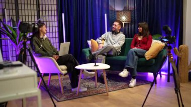 Profesyonel kameralar ve mikrofonlarla rahat bir stüdyoda oturan üç genç içerik yaratıcısı sosyal medya takipçileri için bir video podcast veya canlı yayın yapıyorlar.