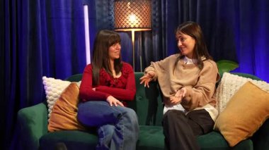 İki neşeli kadın içerik yaratıcısı rahat bir kanepede oturup sohbet ederken bir video podcast veya talk show bölümünü birlikte profesyonel bir yayın stüdyosunda çekiyorlar.