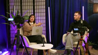 İçerik yaratıcıları profesyonel bir stüdyoda video yayını veya röportaj yaparken kadın mikrofona tutkuyla konuşurken erkek canlı yayında dikkatle dinliyor.