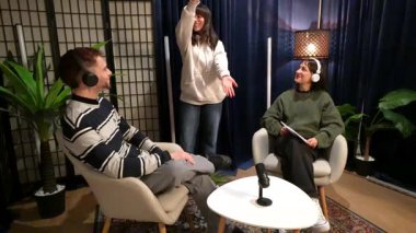 Genç bir adam ve kadın koltuklarda oturup canlı yayın podcast 'i ya da röportajı kaydederken, bir arkadaş arka planda dans ediyor ve sonra setten ayrılıyor.