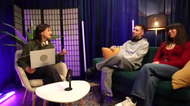 Genç bir kadın podcaster modern bir kayıt stüdyosunda bir adam ve bir kadınla röportaj yapıyor. Etkilenenler ekibi sosyal medya kanalları için yeni dijital içerik üzerinde işbirliği yapıyor
