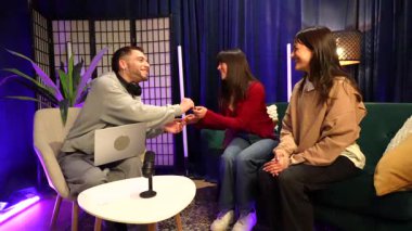 Genç içerik yaratıcısı ilgi çekici bir talk show sunuyor, profesyonel olarak aydınlatılmış bir stüdyoda iki kadınla röportaj yapıyor, sosyal medya izleyicileri için internetten eğlenceli bir bölüm kaydediyor.