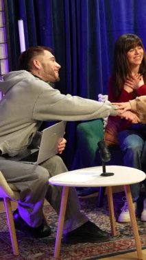 Üç genç içerik yaratıcısı canlı bir şov için konuşmaya başlıyor, el sıkışıyor ve profesyonel ışıklandırma ve ses ekipmanlarıyla modern bir stüdyo ortamında mikrofona konuşuyorlar.