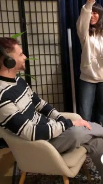 Canlı yayın sırasında mikrofonlara konuşan erkek ve kadın kulaklık takıyor, bir podcast bölümü veya sosyal medya kanalları için samimi ve modern bir stüdyoda bir röportaj kaydediyorlar.