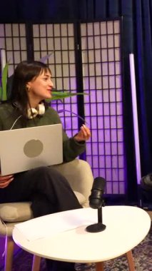 İki gülümseyen içerik yaratıcısı, bir adam ve bir kadın, canlı yayın sırasında mikrofona konuşuyorlar, modern bir kayıt stüdyosunda seyirciler için ilgi çekici içerikler yaratıyorlar.