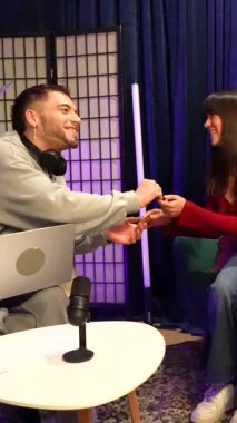 Erkek sunucu podcast röportajına başlamadan önce iki kadın konuk ile tokalaşıyor ya da modern bir stüdyoda neon ışıkları, profesyonel bir mikrofon ve bir dizüstü bilgisayarla canlı yayın yapıyor.