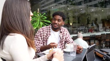 Büyüleyici, genç, ırklar arası bir çift açık bir kafede buluşuyor, kahve içiyor ve birlikte tablet okuyorlar.