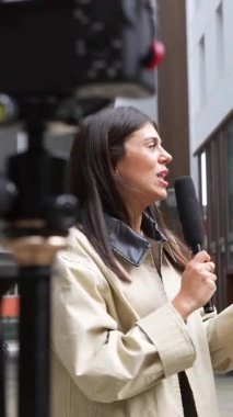 Profesyonel kadın muhabir elinde mikrofonla şehirde bir sokakta genç bir adamla vox pop röportajı yapıyor ve bir haber yayını ya da sosyal medya içeriğiyle ilgili güncel olayları tartışıyor.