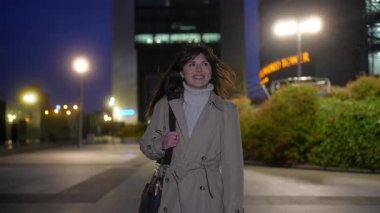 Güzel bir iş kadını, başarılı bir iş gününden sonra laptopuyla ofisten eve giderken güler yüzle modern bir şehirde güvenle yürüyor.