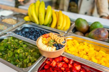 Muz, yabanmersini, çilek, kivi, mango, fındık ve fıstık ezmesi ile kaplı Acai smoothie kasesi, canlı bir self-servis meyve barında sunuluyor.