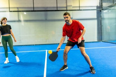İki oyuncu, beyaz çizgili mavi bir sahada, aktif yaşam tarzları için atletik hareket, odaklanma ve eğlence amaçlı uygunluğu gösteren, dinamik bir kapalı top maçında yarışıyor.