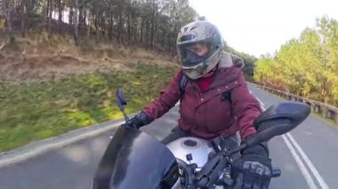 Deneyimli bir kadın kask ve koruyucu giysiler giyerek virajlı asfalt yolda ustalıkla motosiklet sürerken kırsal bir yolculuğun özgürlüğünün ve macerasının tadını çıkarıyor.