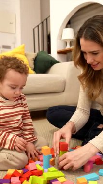 Mutlu anne ve küçük oğlu yerde birlikte oynuyorlar. Ahşap bloklarla renkli bir kule inşa etmek. Ama çocuk devirmekten zevk alıyor. Evde yaratıcılığı teşvik eden ve bağ kuran aile oyun zamanı