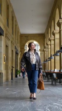 Deri ceketli ve kot pantolonlu neşeli güzel bir kadın şehirdeki klasik bir taş atari salonunda kameraya doğru güvenle yürüyor. Alışverişin ya da gezinin keyfini çıkarıyor.