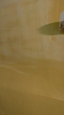 Profesyonel dövmeli otomobil tamircisi boyamadan önce araba yüzeyindeki zımpara doldurucuyu dikkatlice zımparalıyor. Aracı tamir atölyesinde yeni bir sona hazırlamak için yörünge zımpara makinesi kullanıyor.