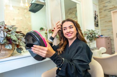 Gülümseyen kadın kuaförde yeni saçını kontrol ediyor, yenilenmiş saç kesiminden, saç kesiminden, kendine güveninden ve özgüveninden tatmin oluyor.