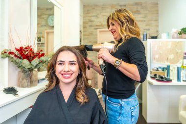 Modern bir güzellik salonundaki yetenekli bir kuaförden profesyonel saç ve saç şekillendirme tedavisi alan mutlu bir müşteri, yenilenmiş ve kendinden emin hissediyor.