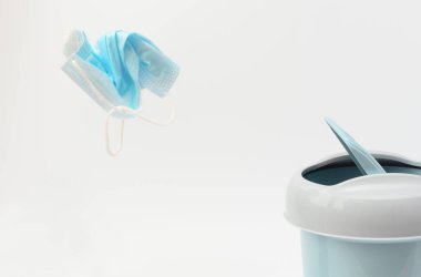 Kırışmış tıbbi koruyucu yüz maskesi beyaz arka planda çöp kutusuna çarpıyor. Karantina ve pandemik konseptin sonu. Sağlıklı yaşam tarzı, normal hayata dönüş.. 