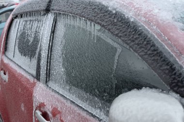 Dondurucu yağmurdan sonra buzla kaplı kırmızı araba. Buz fırtınası kasırgasından sonra her şeyi kapladı. Doğanın korkunç güzelliği. Kış zamanı. Seçici odak. 