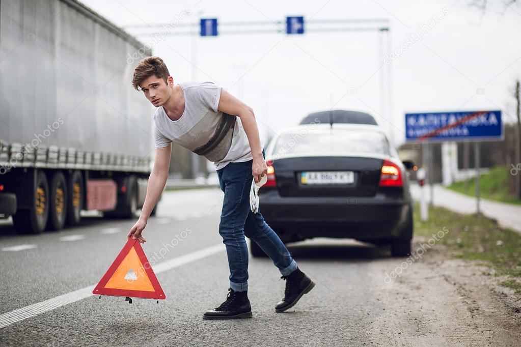 car with breakdown alongside the road, man sets warning triangle
