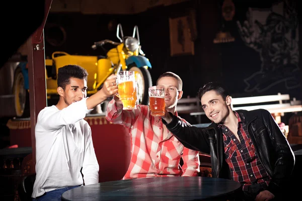 Happy friends clinking with beer mugs in pub, smiling. — Stock Photo, Image