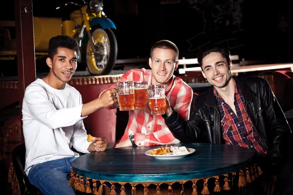 Amigos felices tintineando con tazas de cerveza en el pub, sonriendo . — Foto de Stock